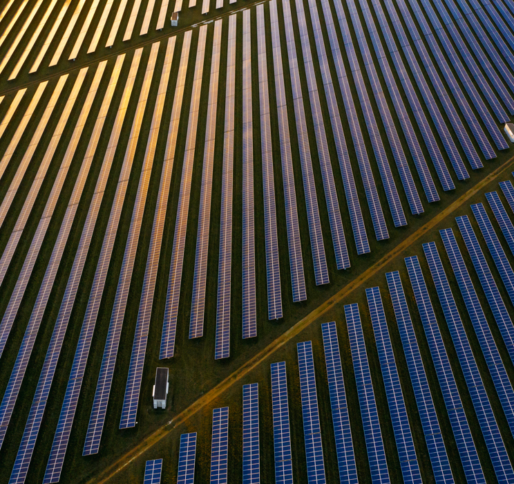 An aerial image of a solar power plant with the sun reflecting in multiple of the panels created  by Unicus. 