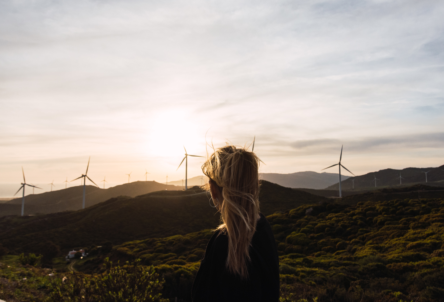 An image of a woman standing in the front looking at a windmill park. 